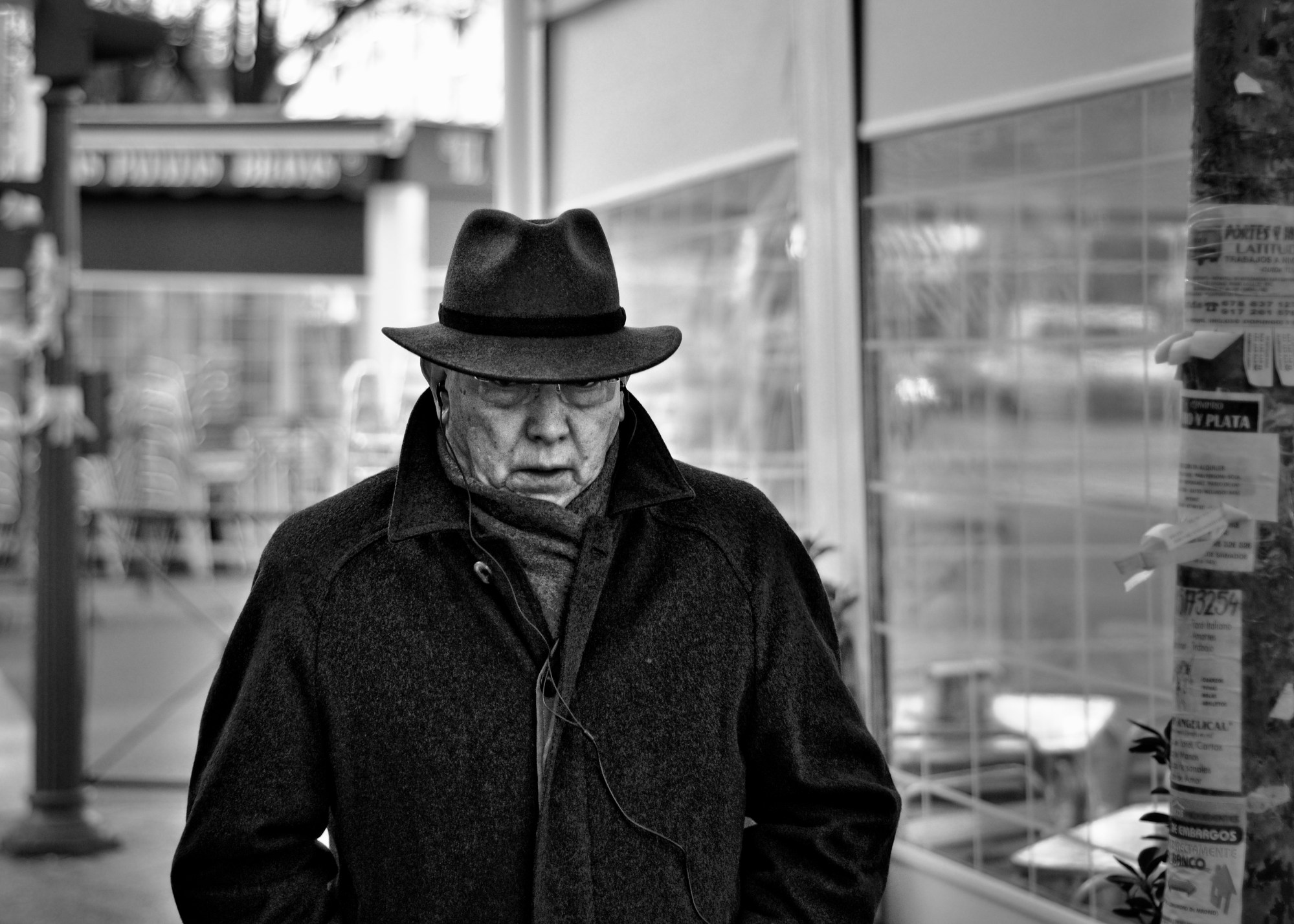 Hombre mayor con sombrero y abrigo oscuro caminando con la mirada baja.