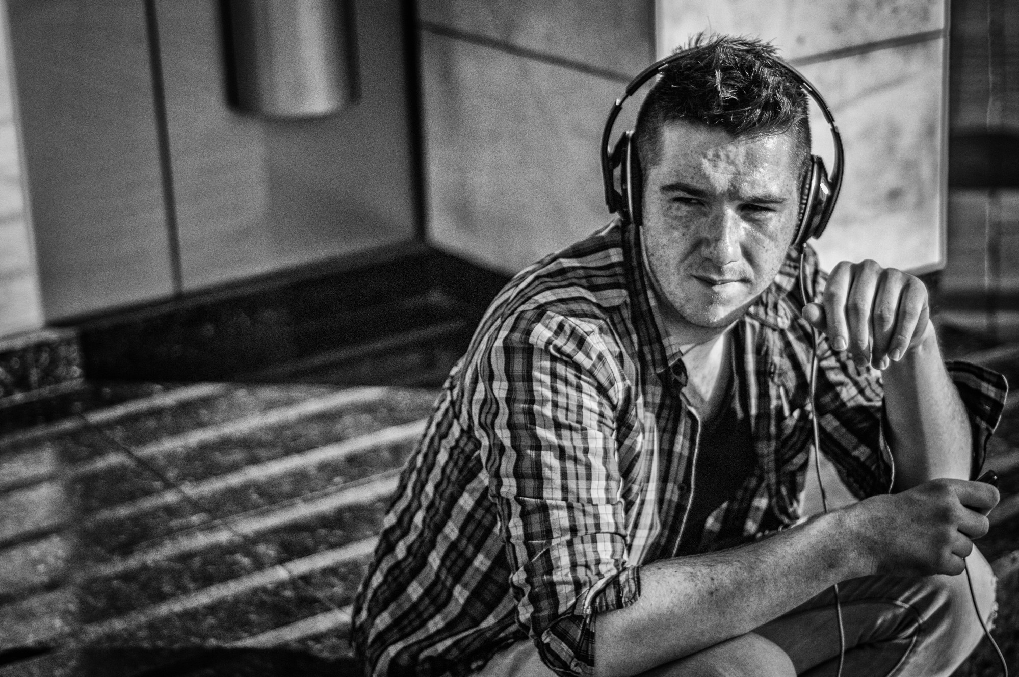 Hombre con auriculares y camisa de cuadros sentado en el suelo, mirando a cámara.