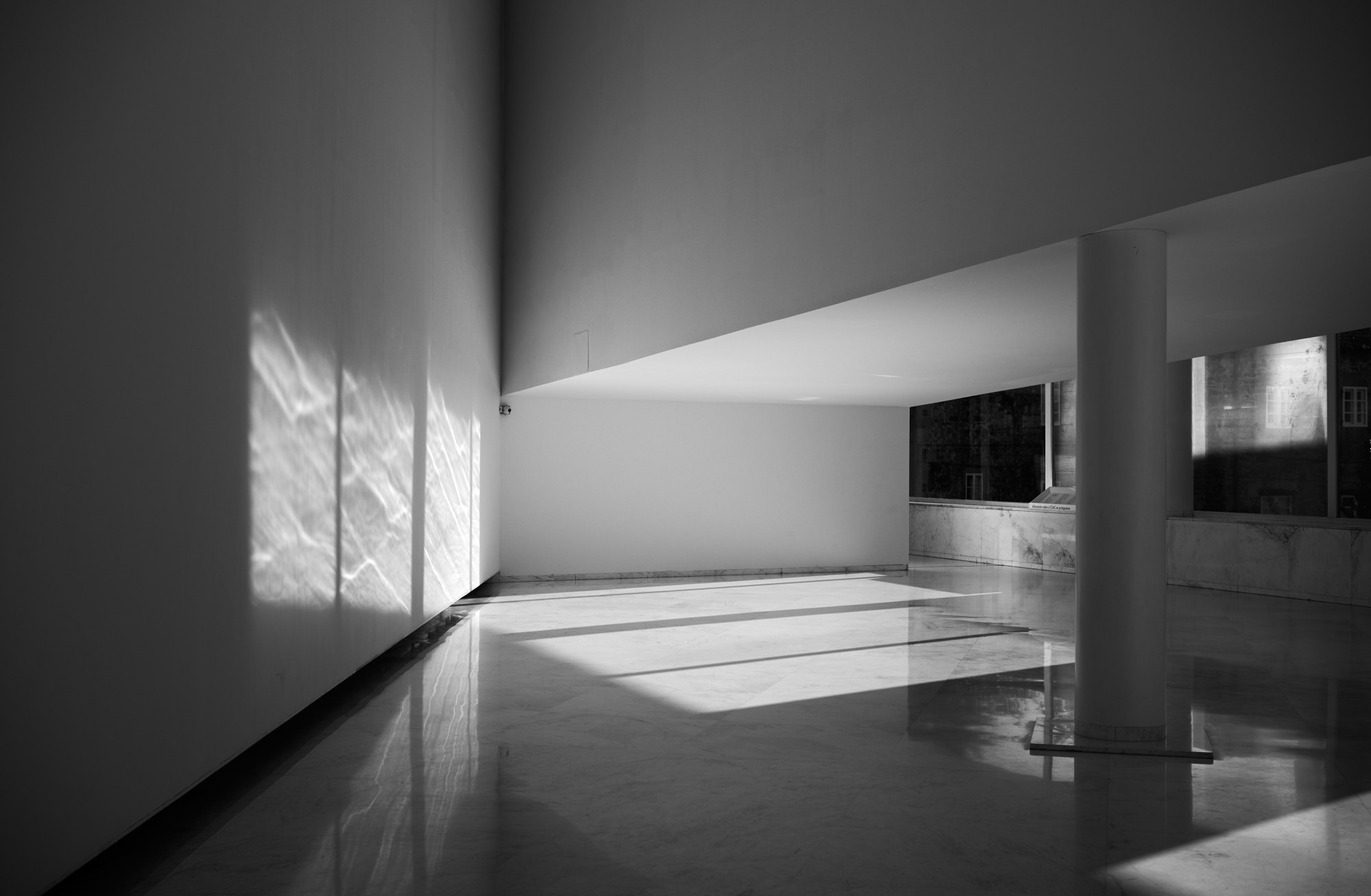Espacio interior vacío con una columna y la luz de una ventana proyectada en la pared.