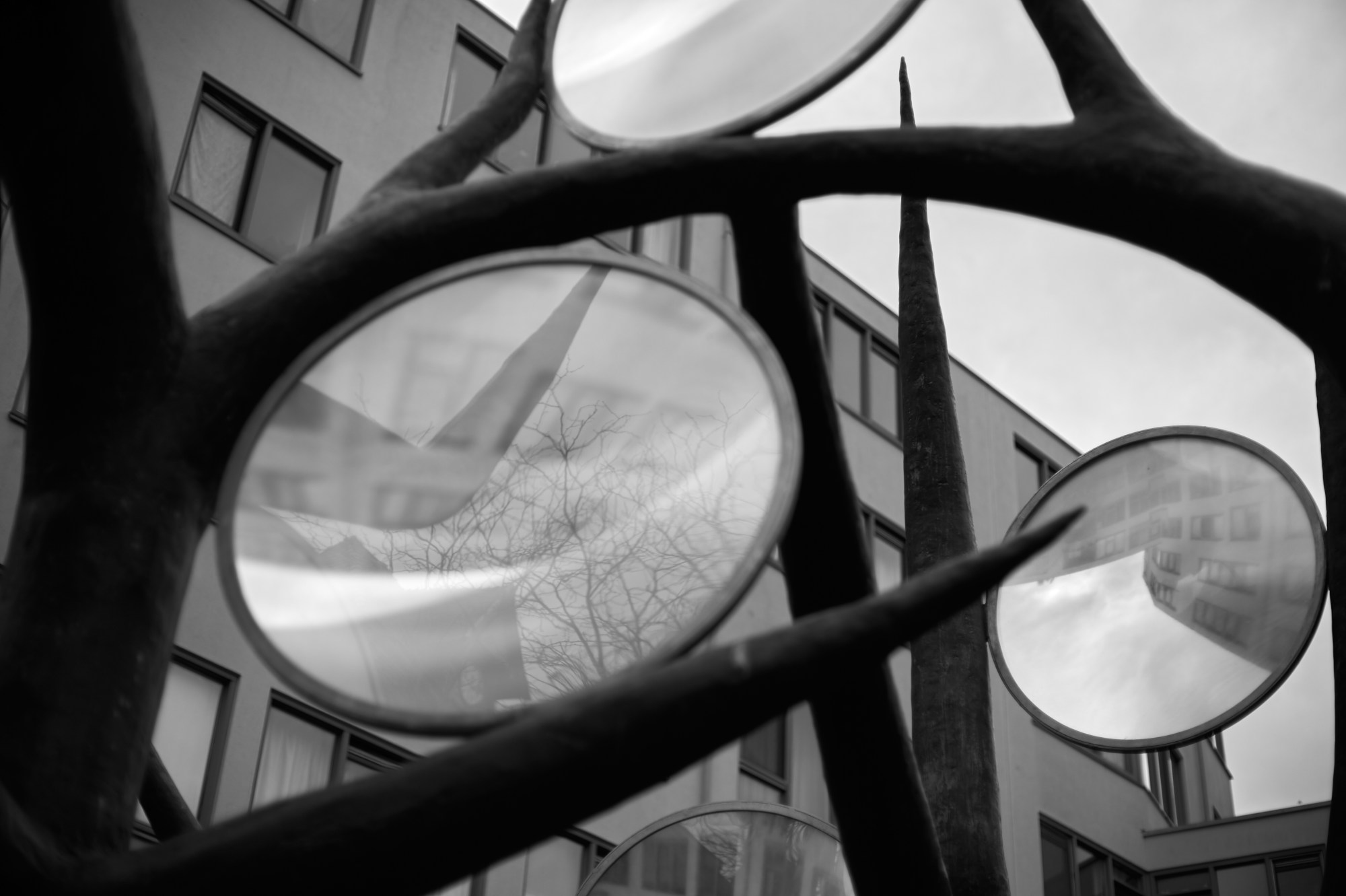 Escultura metálica con grandes lentes circulares ante un edificio.