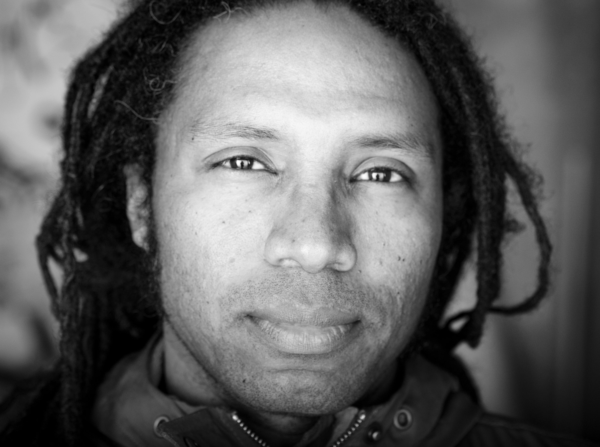 Primer plano del rostro de un hombre con rastas, mirando a cámara.