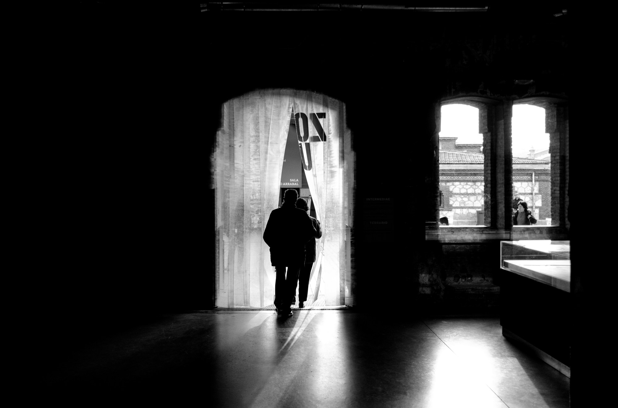 Silueta de una persona cruzando una puerta con cortina, en un interior oscuro.