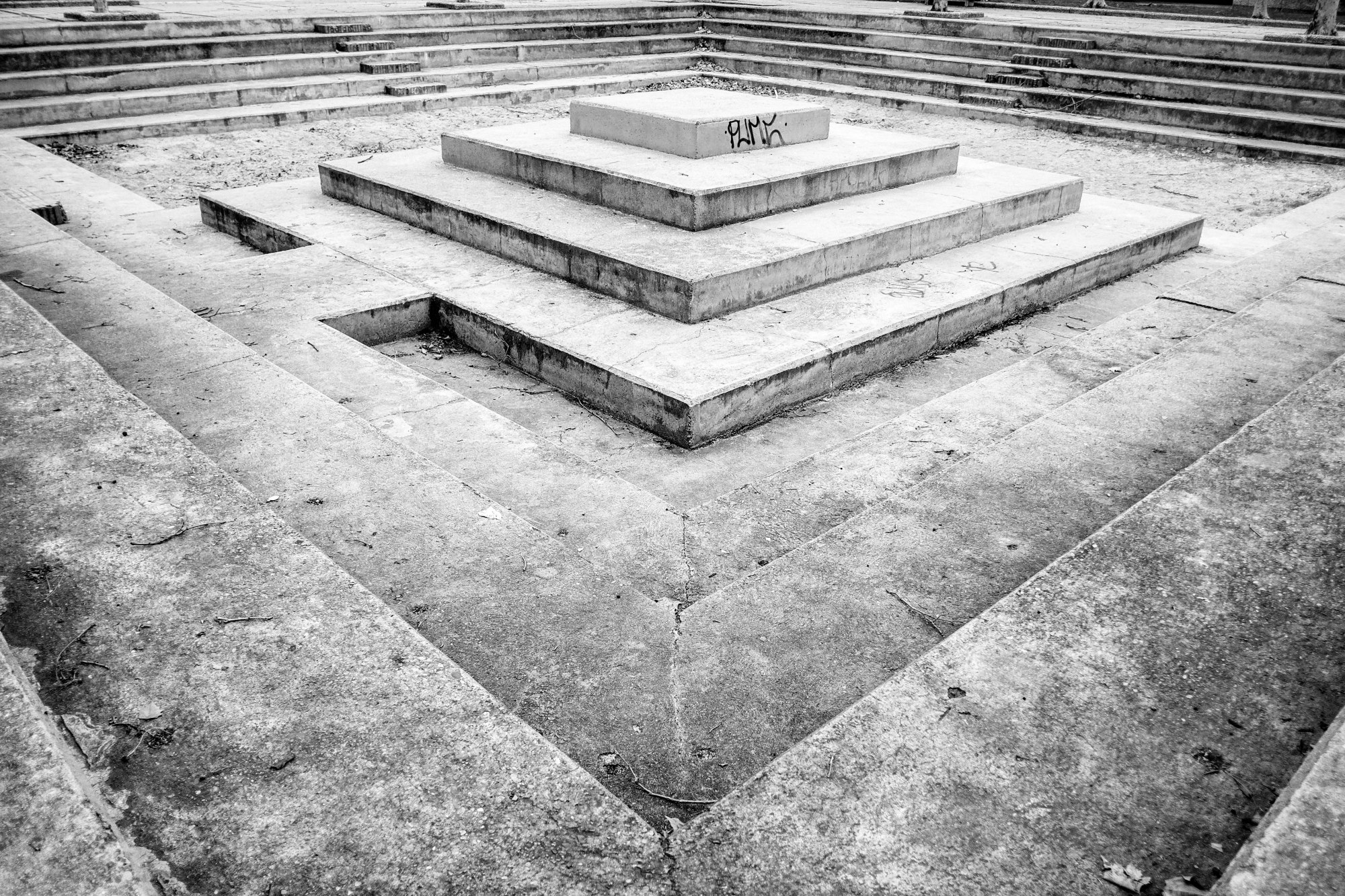 Plataforma escalonada de piedra en el centro de una plaza hundida con gradas.