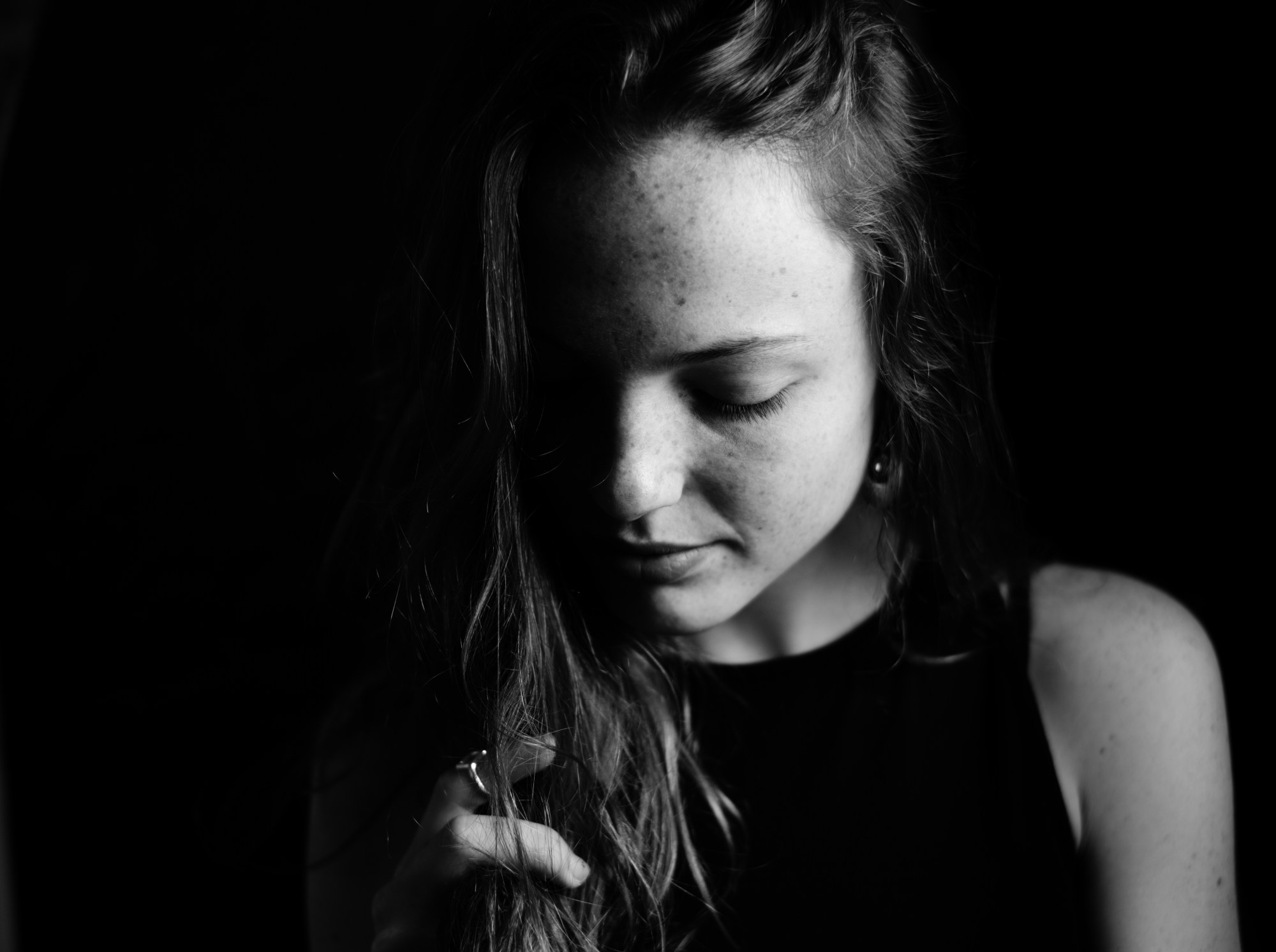 Retrato de mujer joven con la mirada baja y medio rostro en sombra.