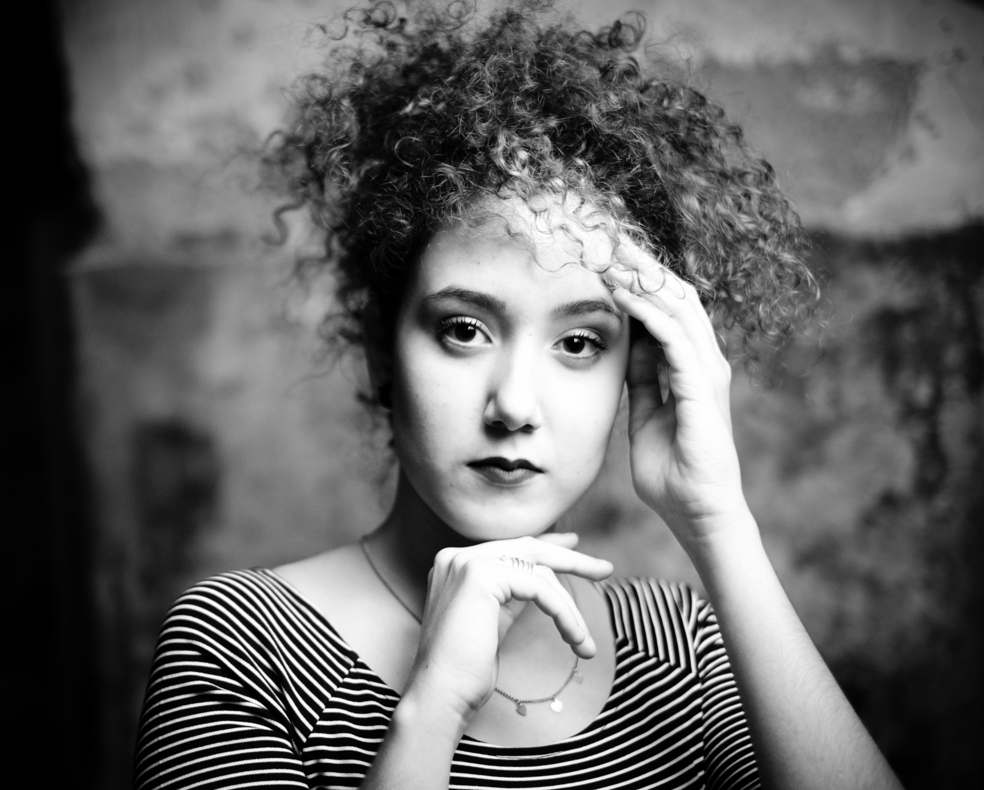 Retrato de mujer joven de pelo rizado con camiseta de rayas, una mano en la frente y otra bajo la barbilla.