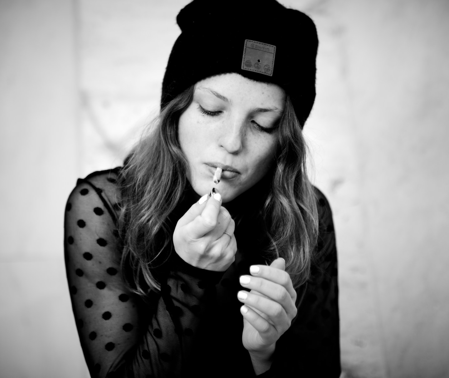 Woman in a wool hat and polka-dot blouse touching up her lipstick.