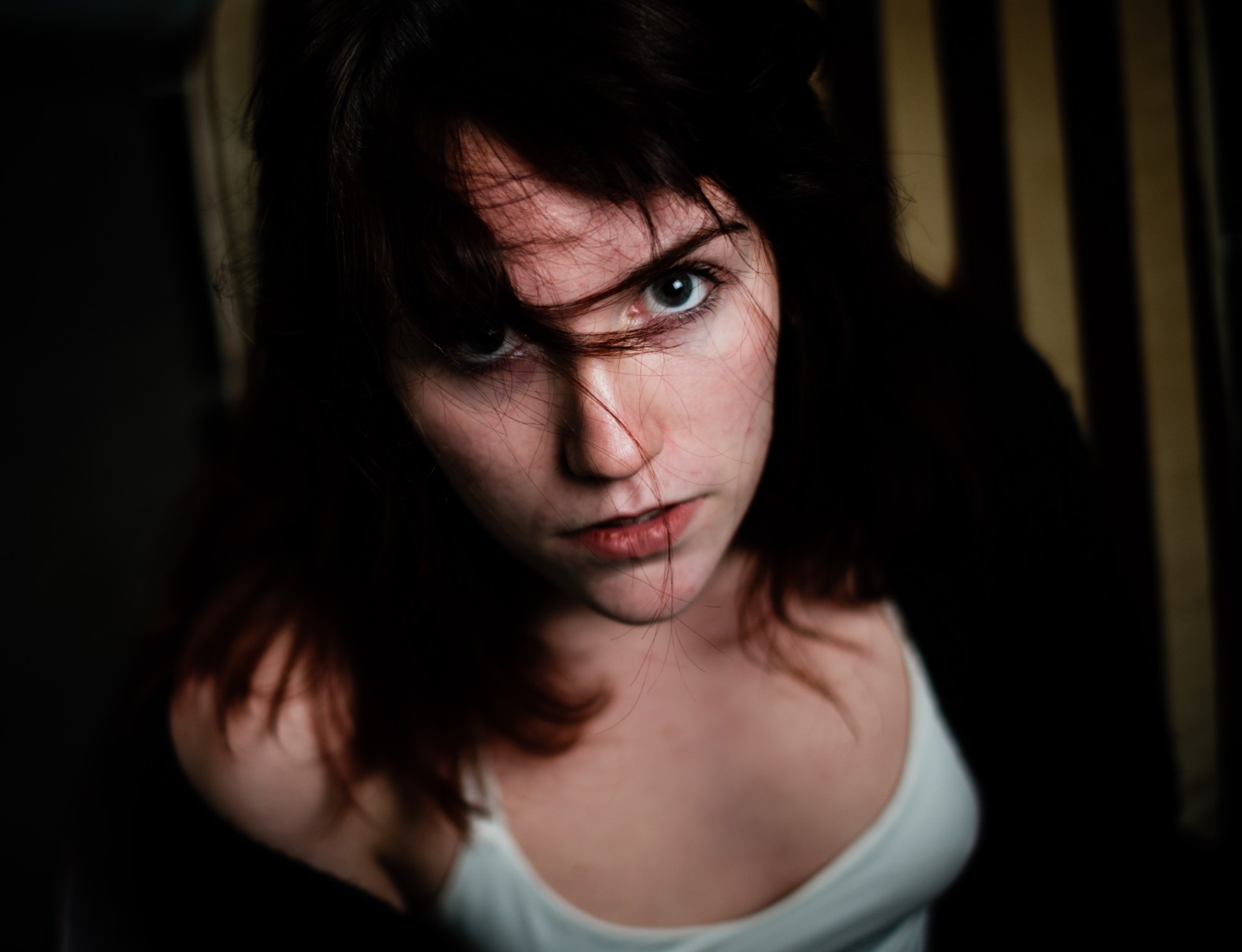 Retrato en picado de una mujer con el pelo sobre la cara y camiseta blanca, mirando a cámara.