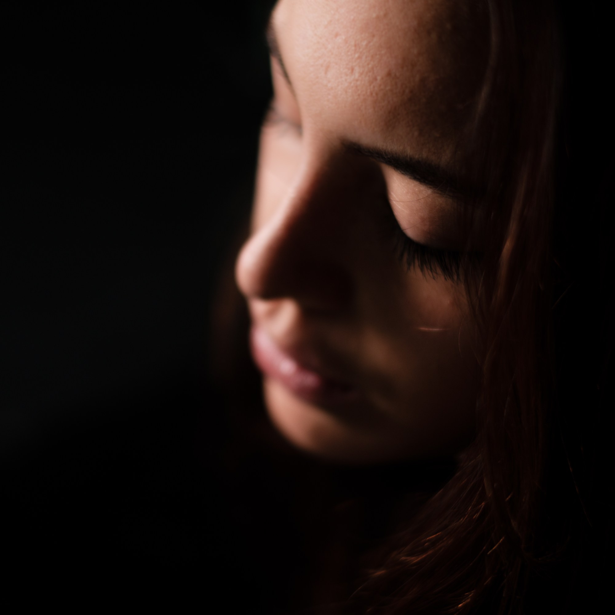 Primer plano de perfil de una mujer con los ojos cerrados, en penumbra.
