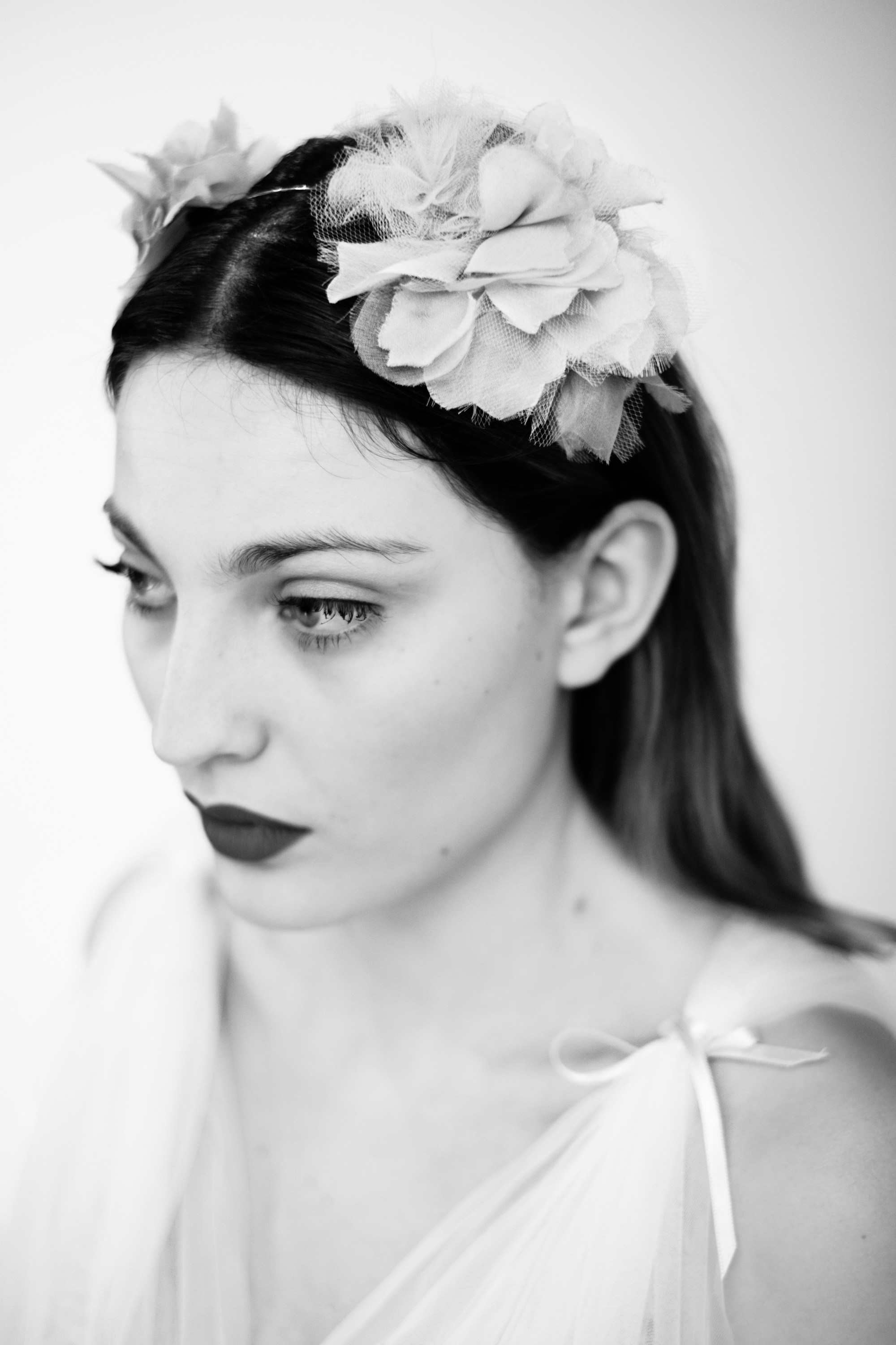 Retrato de mujer joven con flores en el pelo y labios oscuros, mirando hacia abajo.