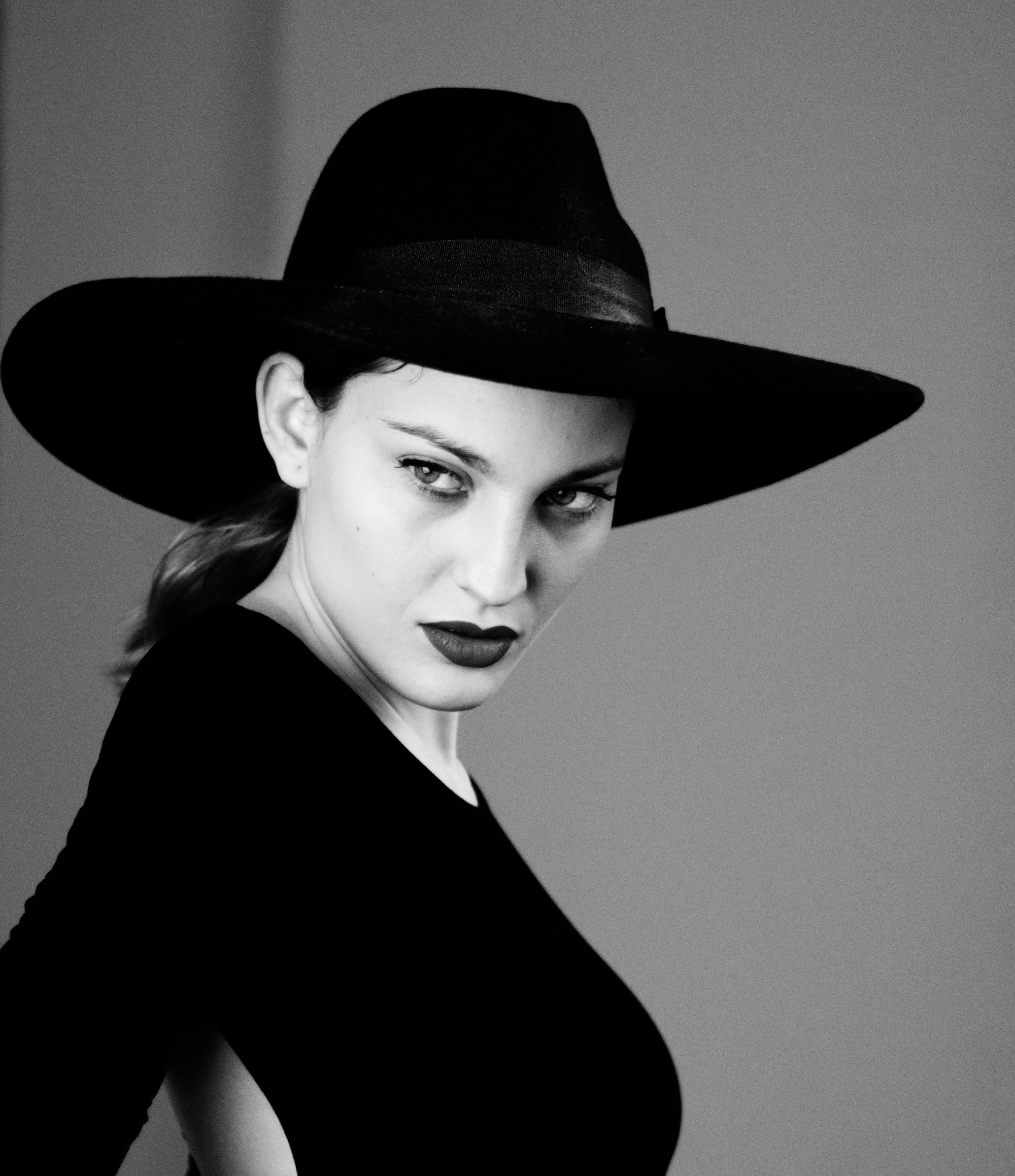 Retrato de mujer con sombrero negro de ala ancha y vestido negro, mirando de lado.