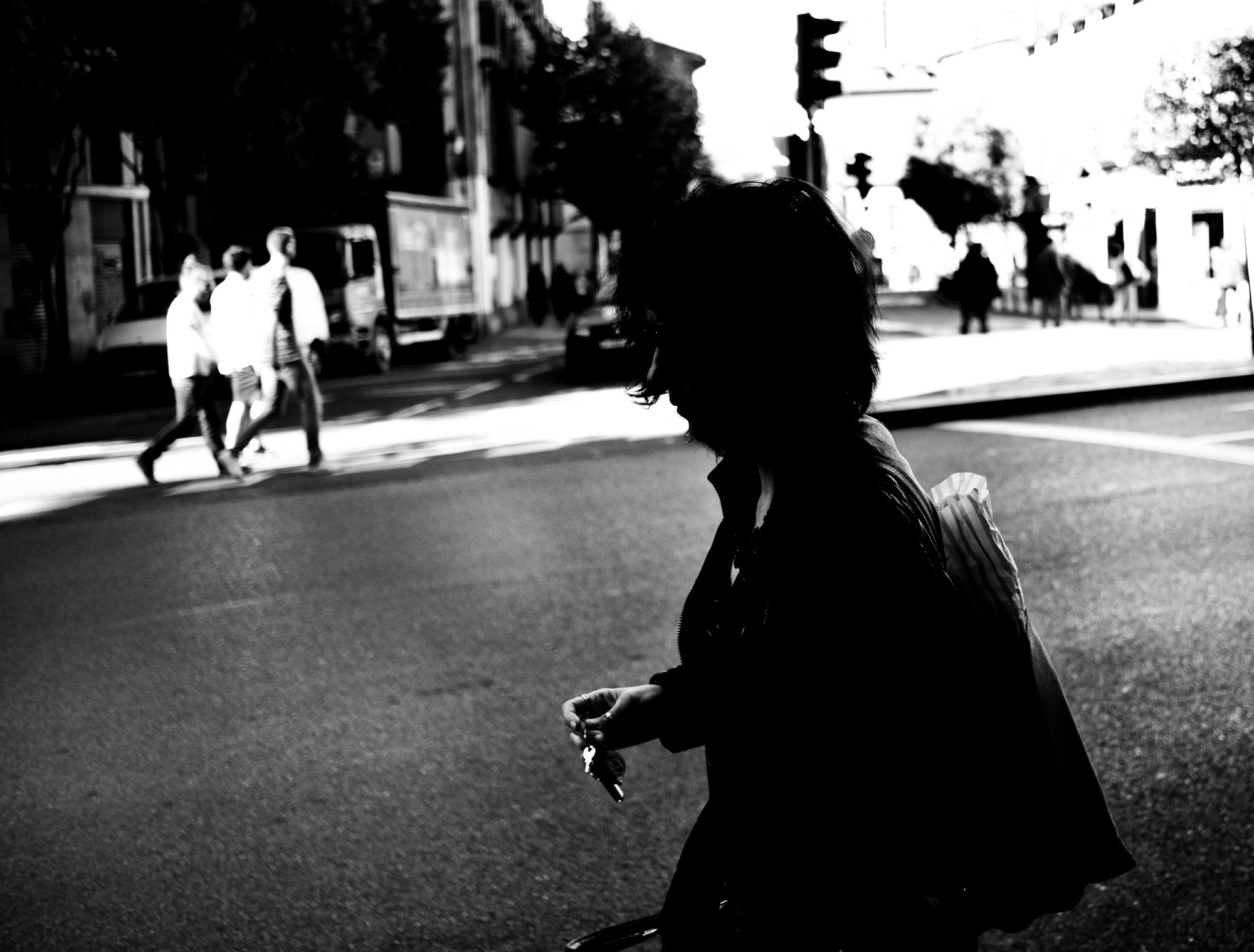 Silueta de una mujer cruzando la calle a contraluz, con peatones al fondo.