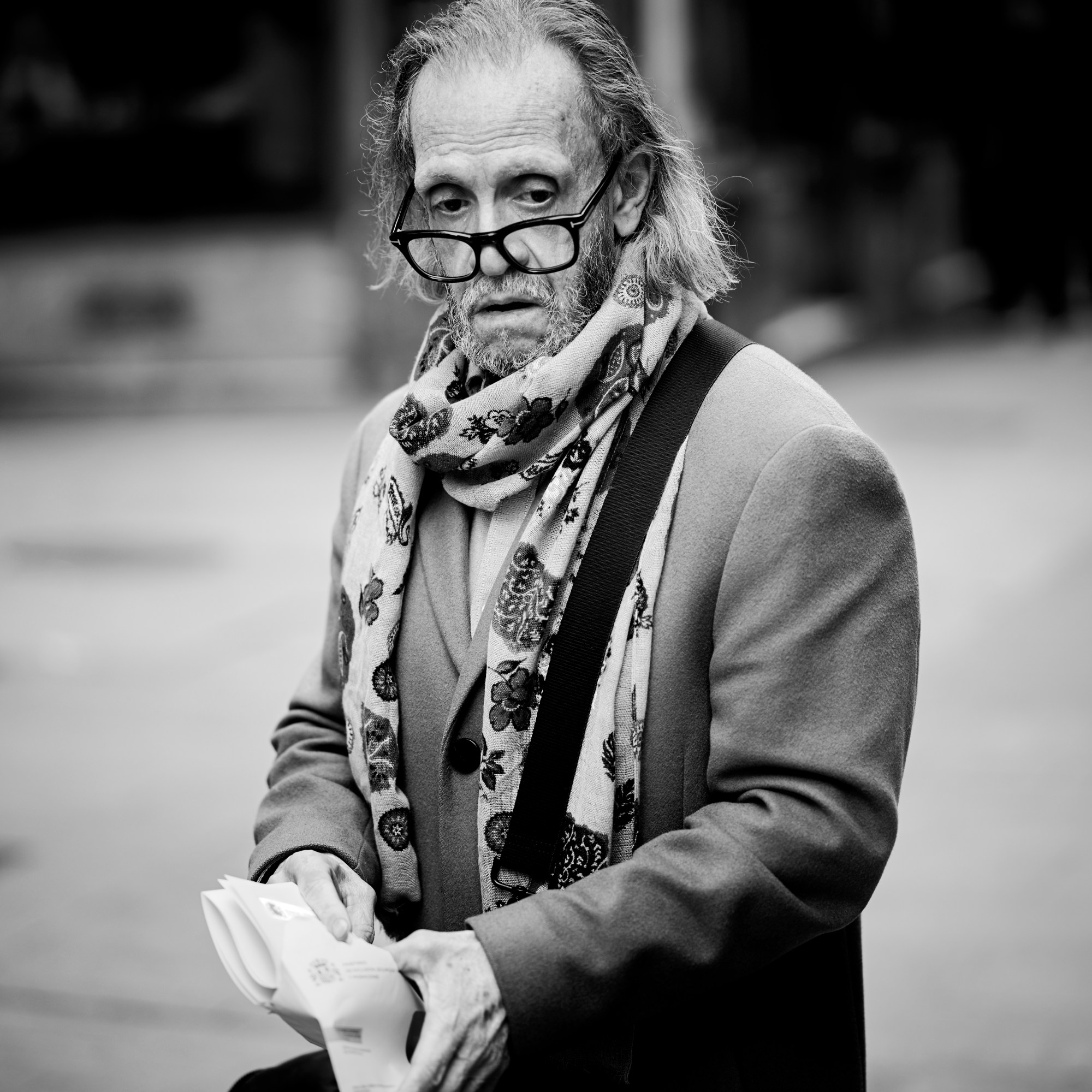 Hombre mayor con gafas, pañuelo estampado y americana mirando algo que sostiene en las manos.