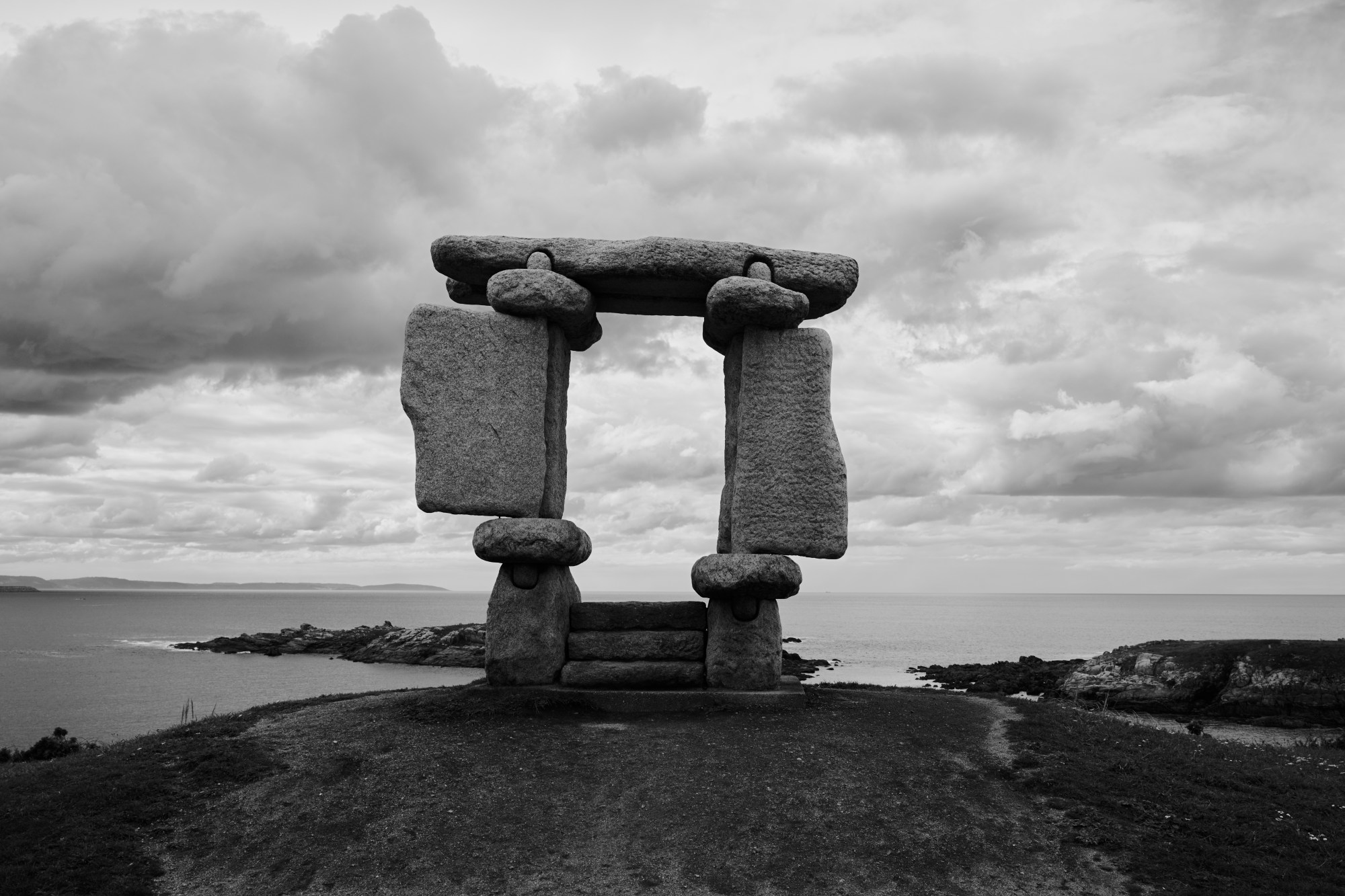 Monumento de piedra en forma de dolmen sobre un promontorio junto al mar.