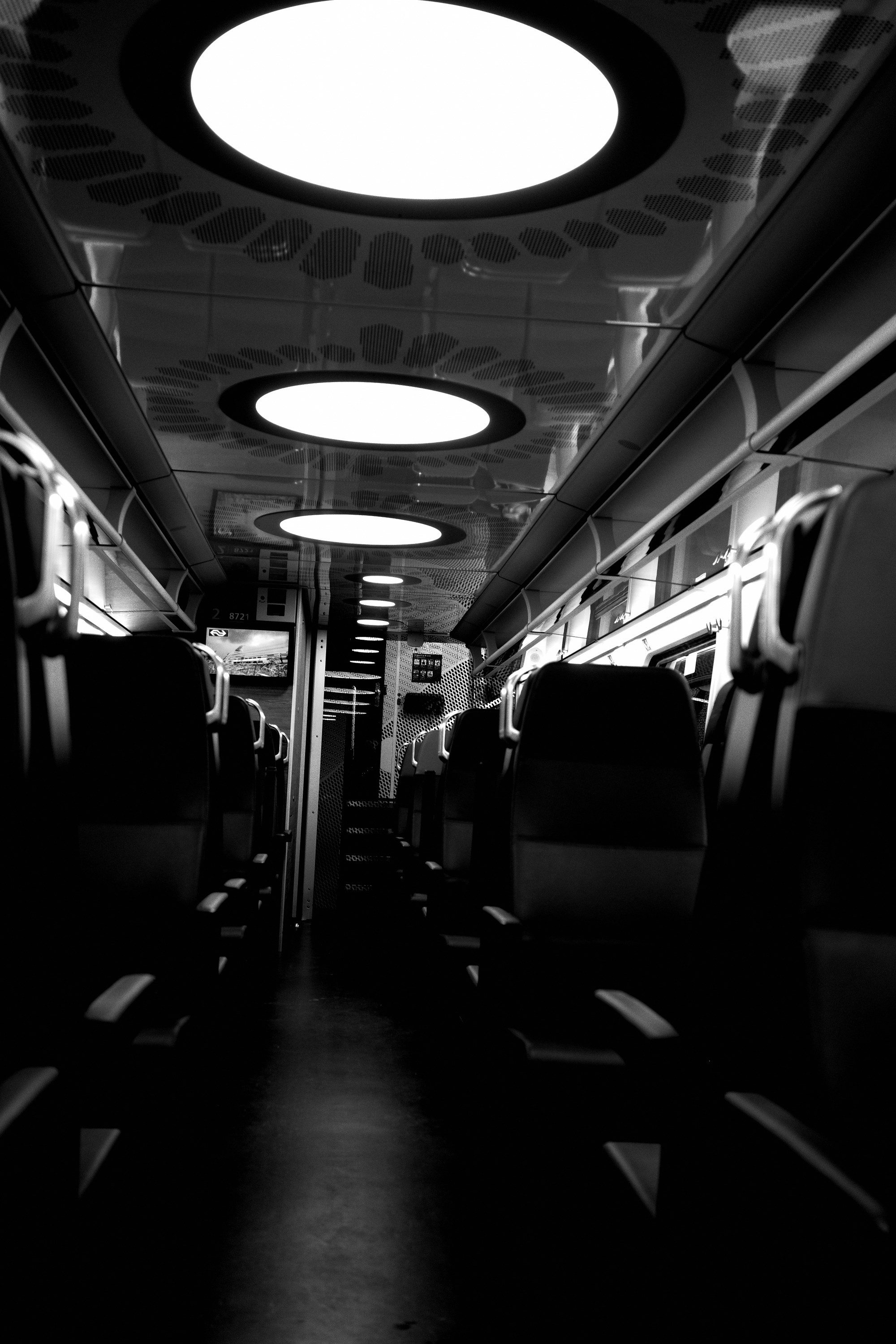 Pasillo de un vagón de tren en penumbra, con plafones circulares en el techo.
